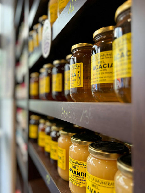 Shelf with jars of honey labeled 'La Muhier' on a blurred background