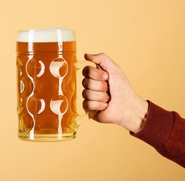 A hand holding a beer in a beer mug on a peachy background