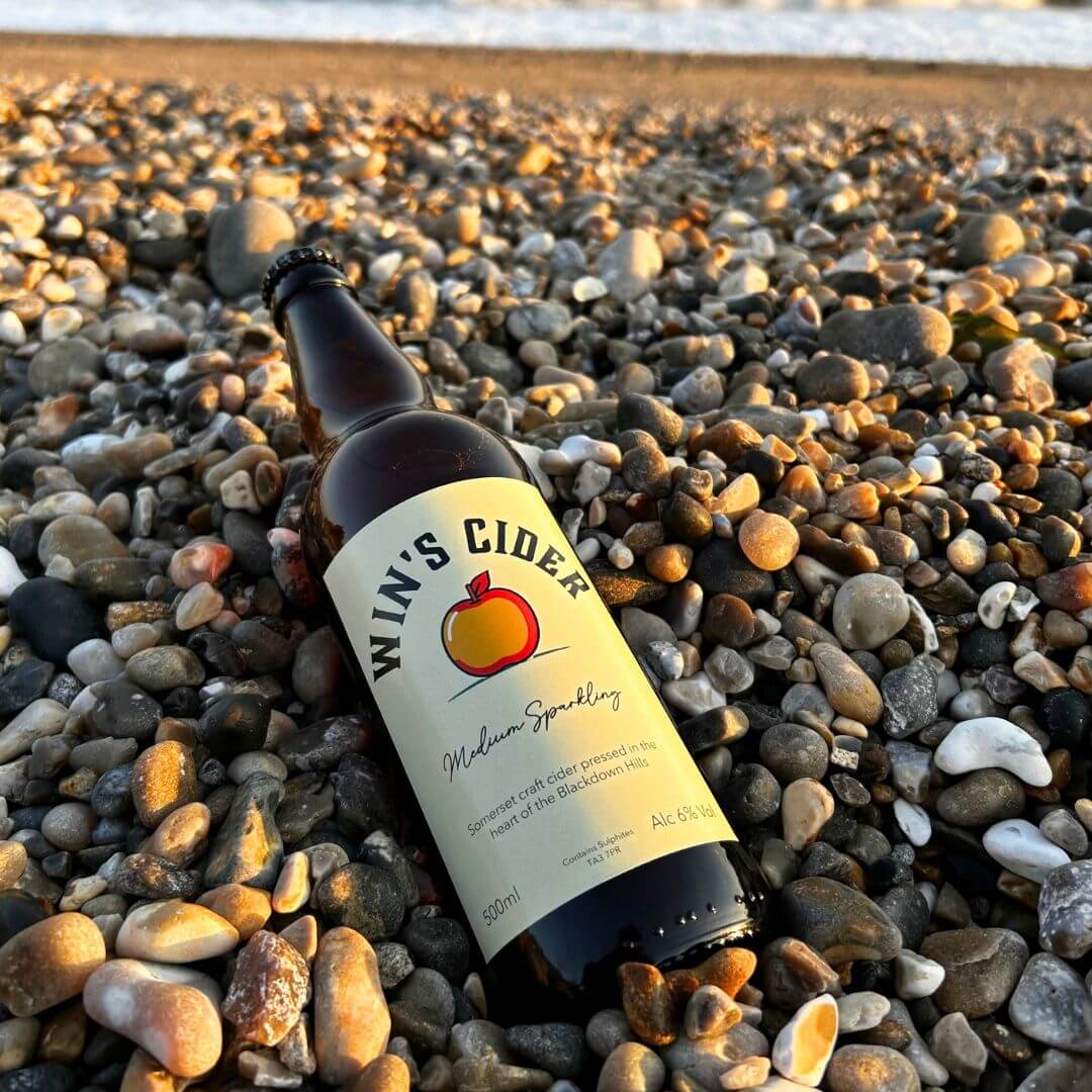 Win's Cider amber cider bottle on a beach
