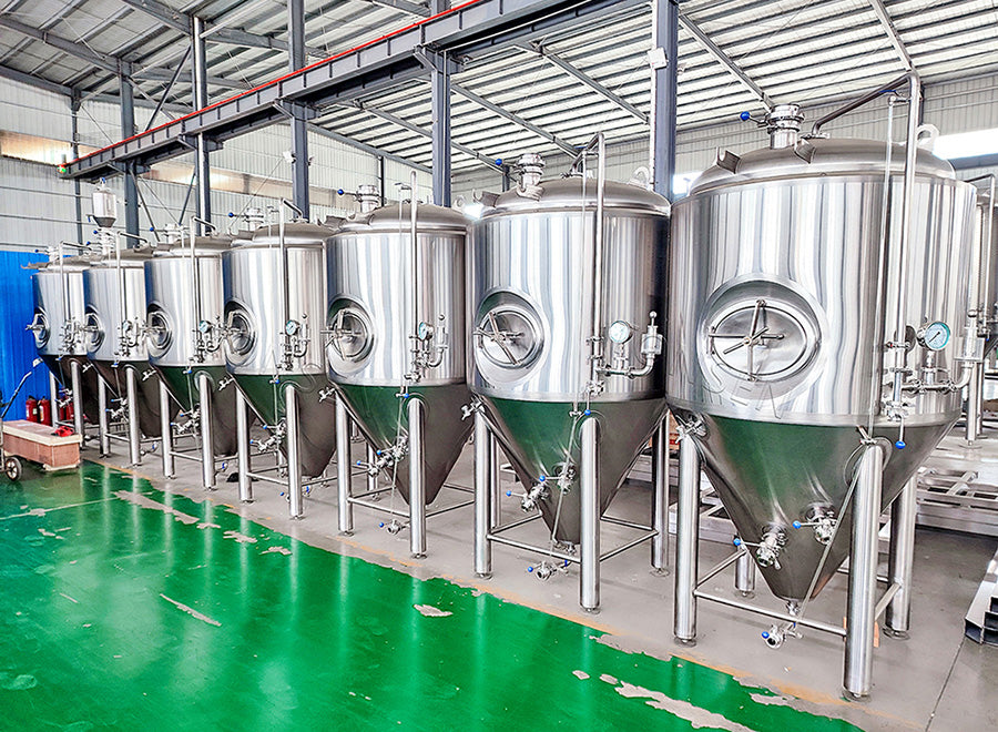 A row of large stainless steel beer fermentation tanks on a green floor