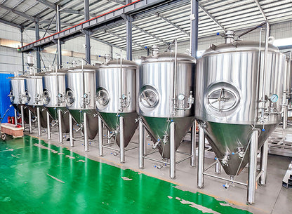 A row of large stainless steel beer fermentation tanks on a green floor