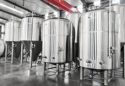 Large stainless steel tanks in a brewery interior with concrete floors and industrial ceiling structures.