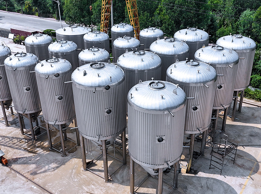 A large outdoor collection of stainless steel fermentation tanks on a concrete lot