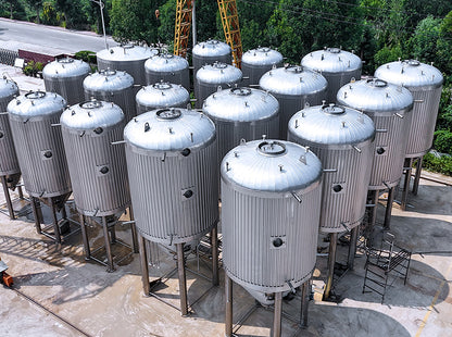 A large outdoor collection of stainless steel fermentation tanks on a concrete lot